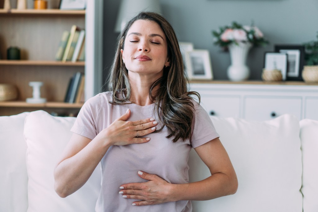 A woman holds her chest while inhaling deeply.