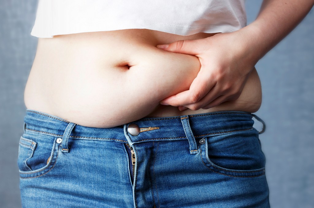 The woman's hand by drinking excessive abdominal fat, symbolizing the concept of overweight