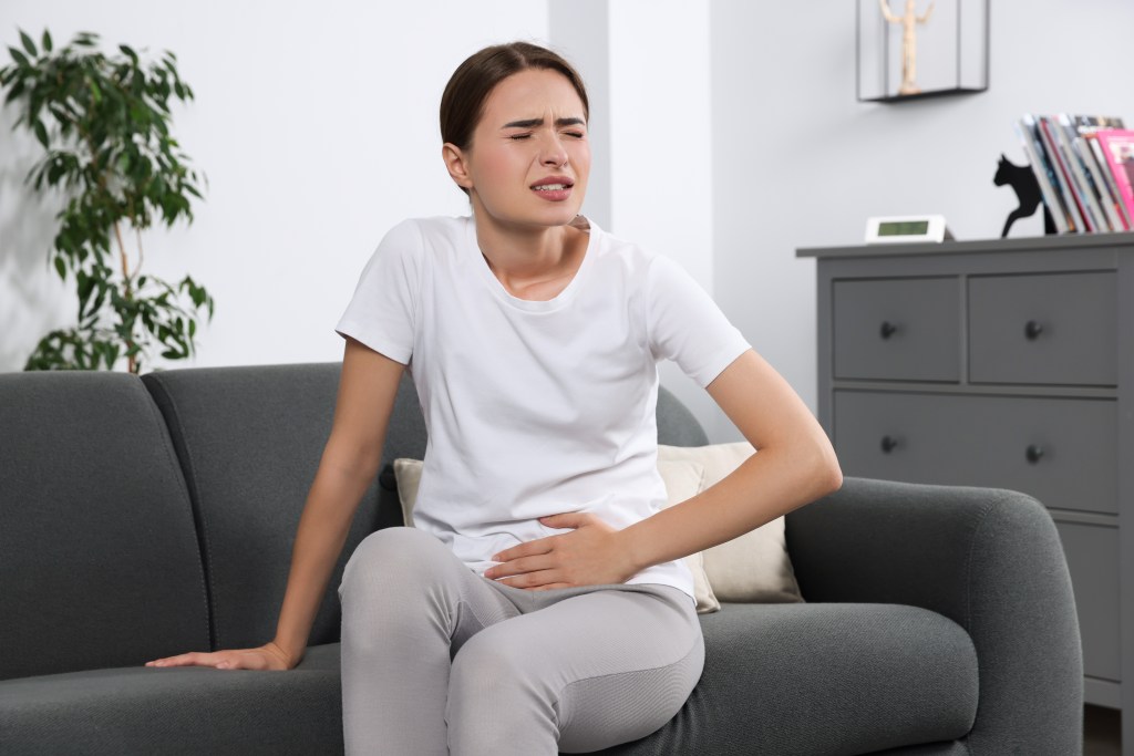 Young woman who experiences colic due to cystitis, sitting on a sofa in the house