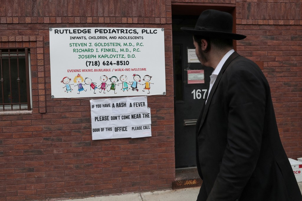 The man in Brooklyn walking a sign warning parents not to bring children with redness and fever to a pediatric office and instead call.
