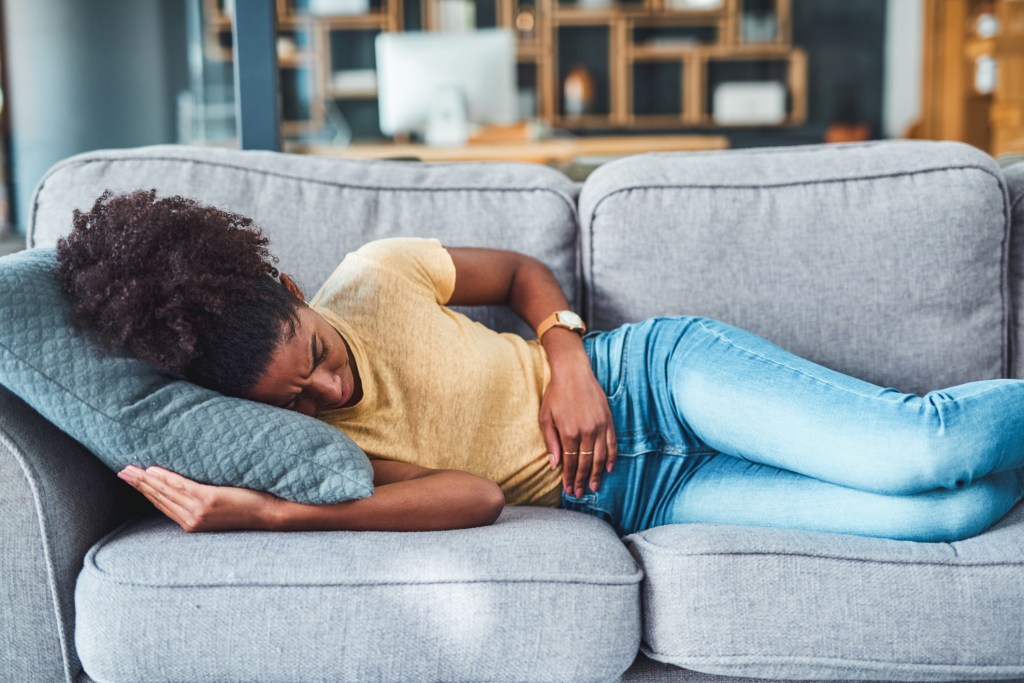 A woman lies in bed holding her lower abdomen while experiencing abdominal pain.