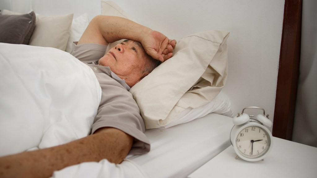 The elderly man lies awake in bed because of insomnia